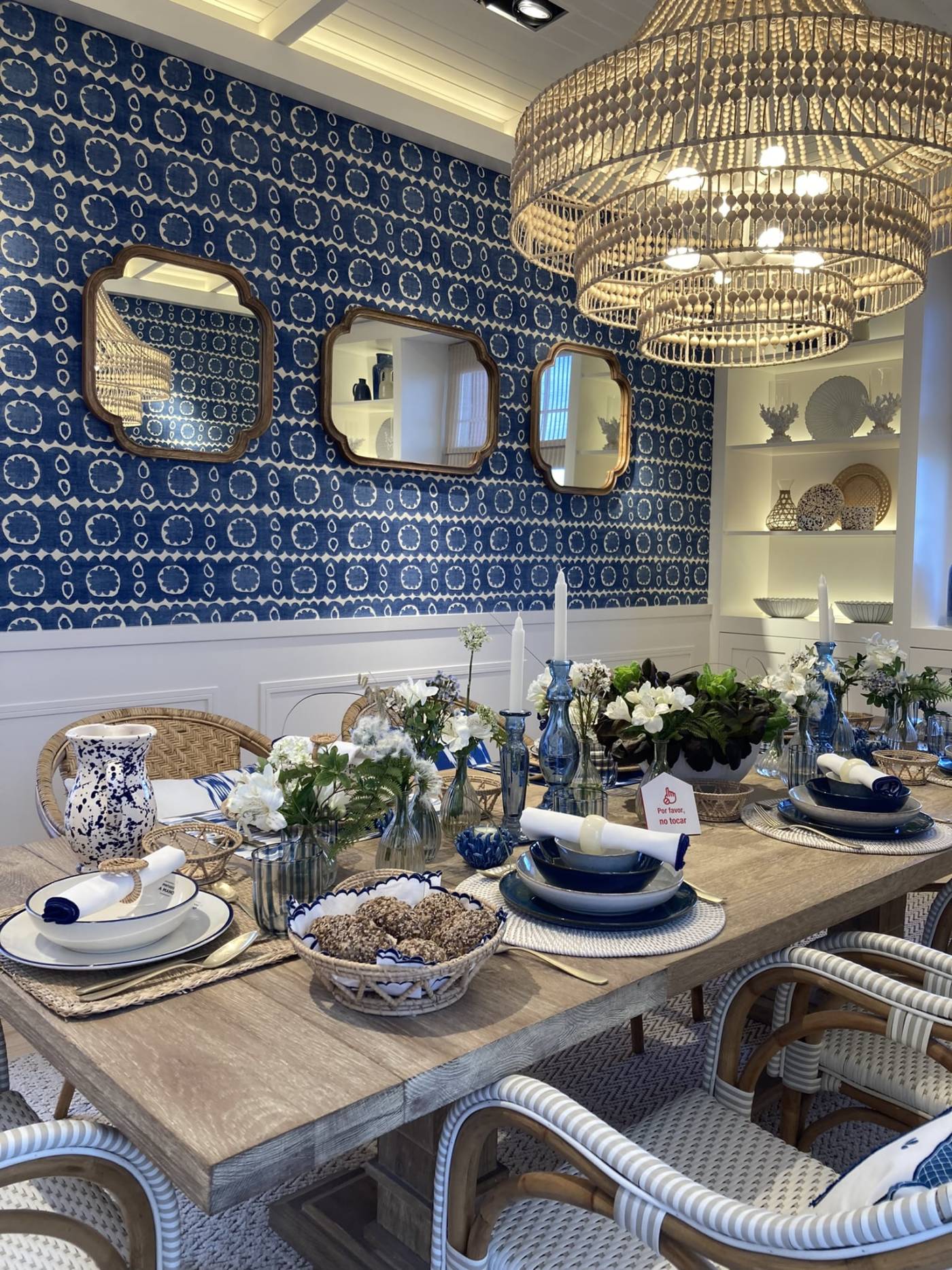 Insight_Header_Casa Decor_Diseño de interiores con mesa de madera, sillas en tonos marrones, blancos y grises, luminarias naturales de mimbre, pared azul con papel pintado, espejos y vajilla en tonos tierra con vegetación