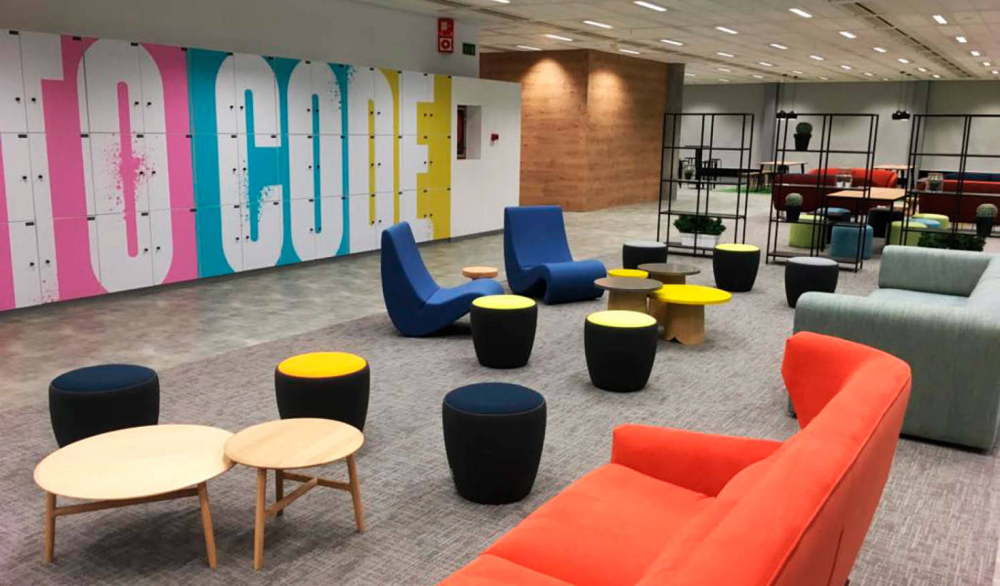 Zona común en espacio de oficinas con mobiliario moderno y colorido, taquillas, y espacio de socialización y descanso común para empleados