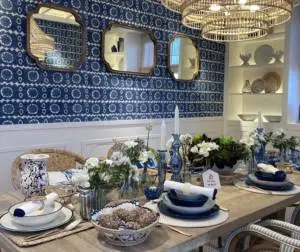 Insight_Header_Casa Decor_Diseño de interiores con mesa de madera, sillas en tonos marrones, blancos y grises, luminarias naturales de mimbre, pared azul con papel pintado, espejos y vajilla en tonos tierra con vegetación