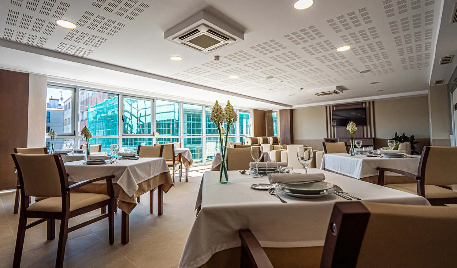 Cafeteria y comedor con tonos beiges e iluminacion natural con cristalera, mesas y sillas